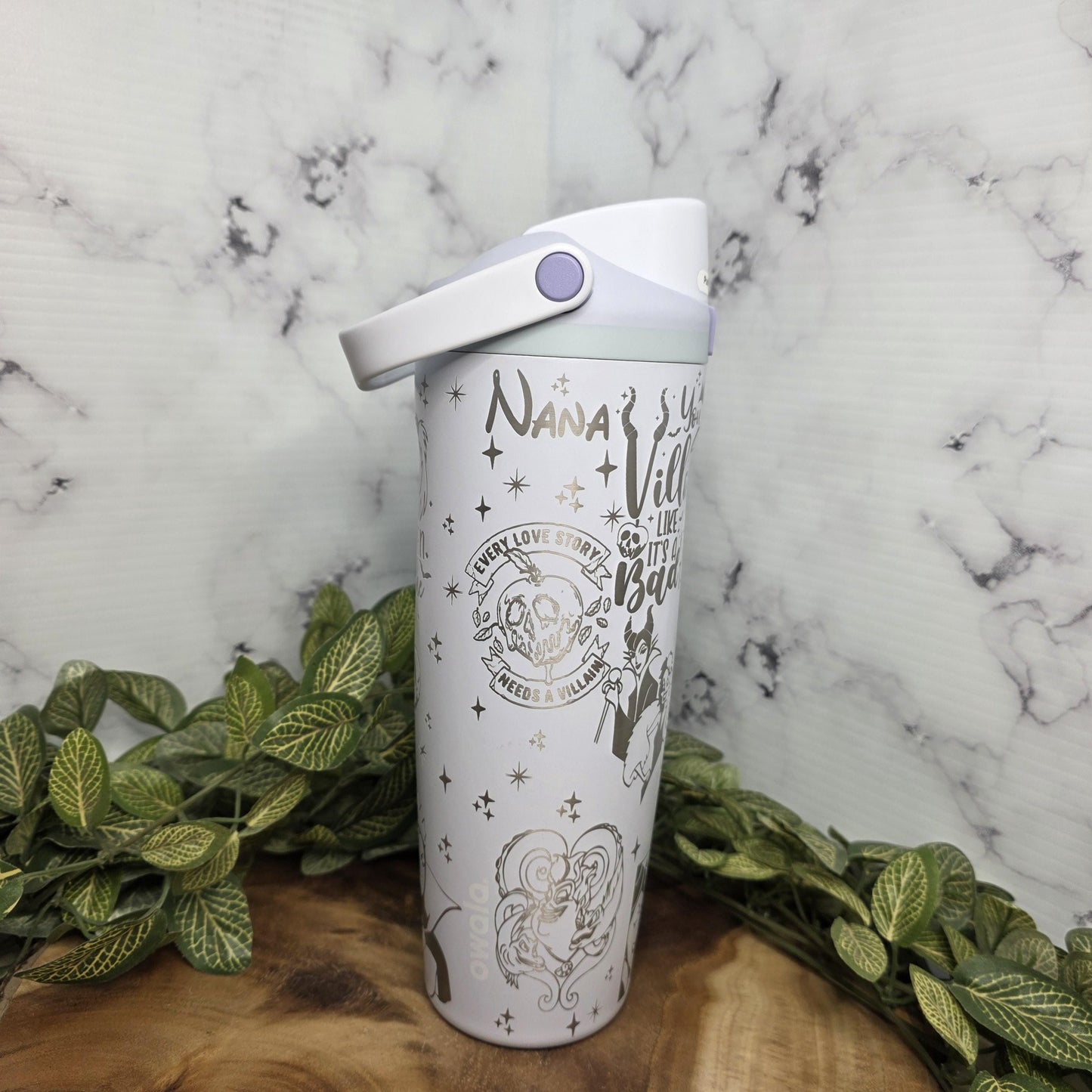 A white water bottle with a decorative design on it, placed on a marble surface surrounded by green leaves.